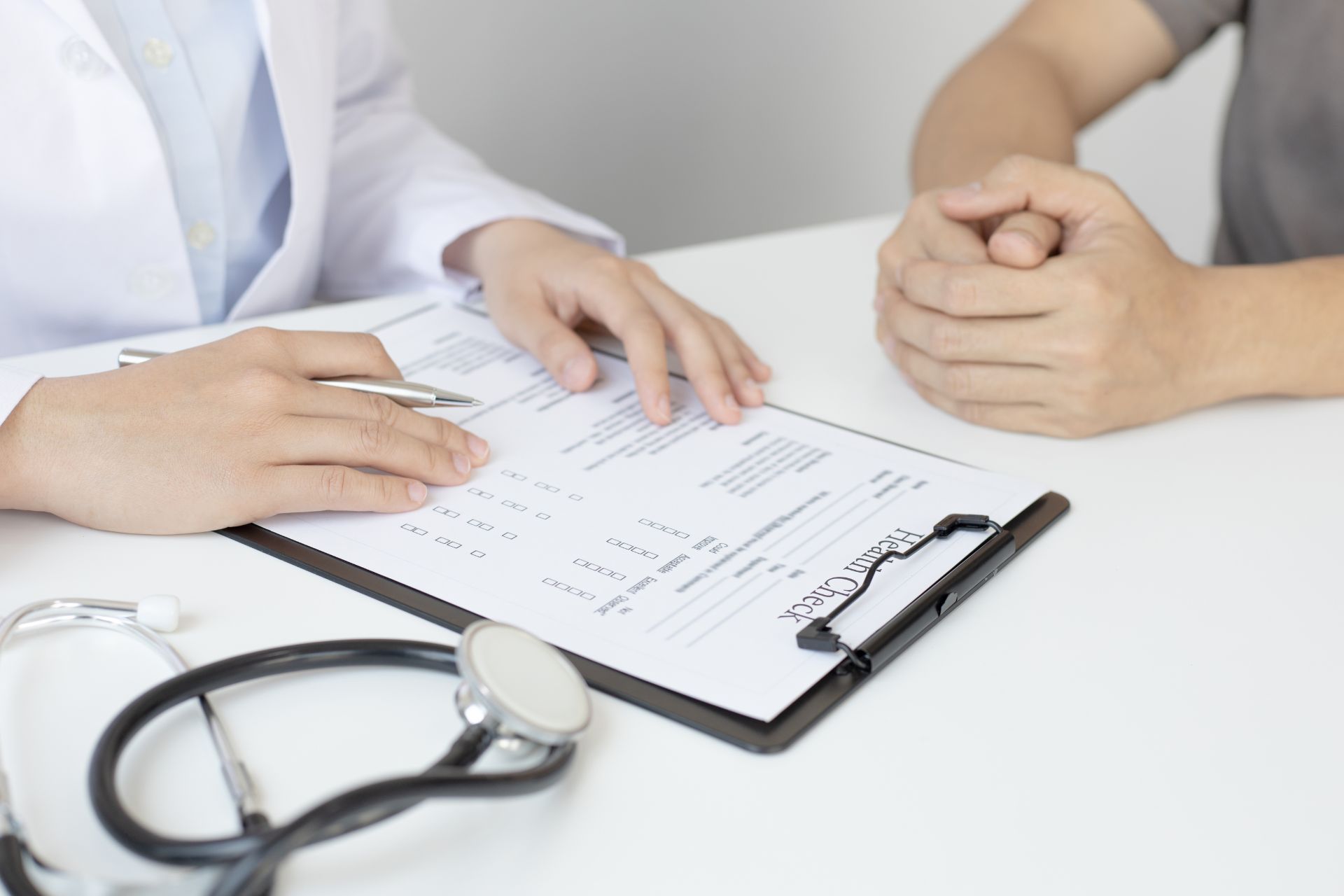 A doctor reviews an important agreement on a clipboard with a patient, who sits with their hands clasped. A stethoscope is on the table, underscoring the significance of their discussion.