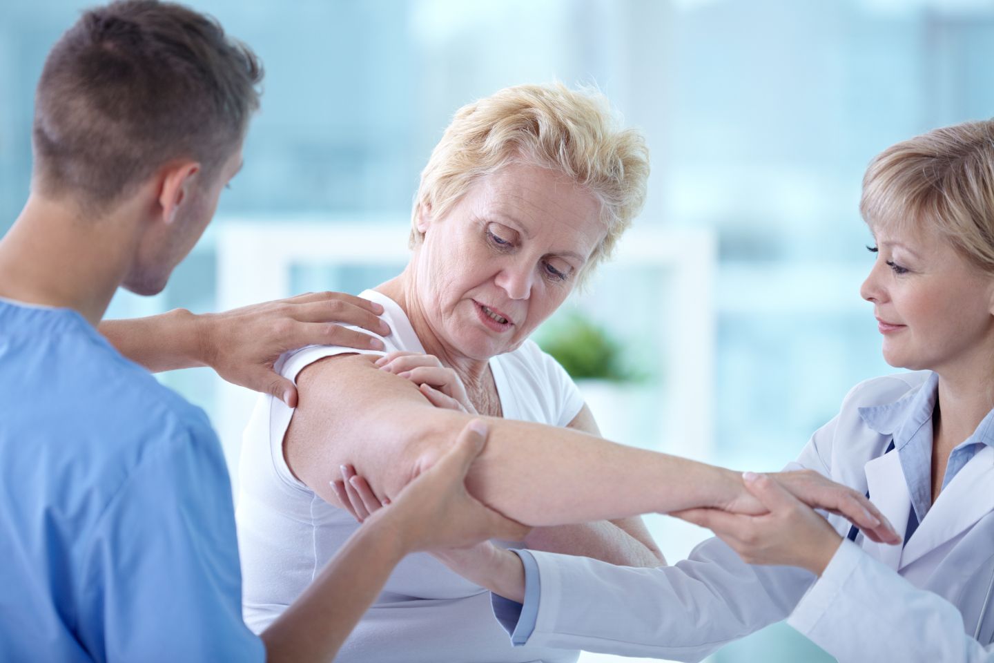 A medical professional, much like a dynamic content specialist, assists an older woman in a white shirt with arm exercises, while another person supports her shoulder.