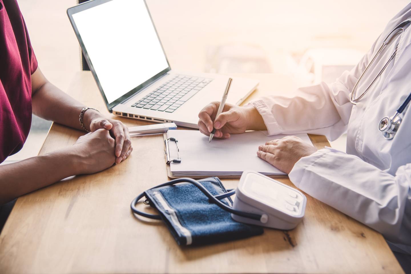 About Us - PointMed: During a consultation, the doctor efficiently writes on a clipboard as they review dynamic content on the laptop. A stethoscope and blood pressure monitor are neatly arranged nearby, ready to ensure comprehensive patient care.