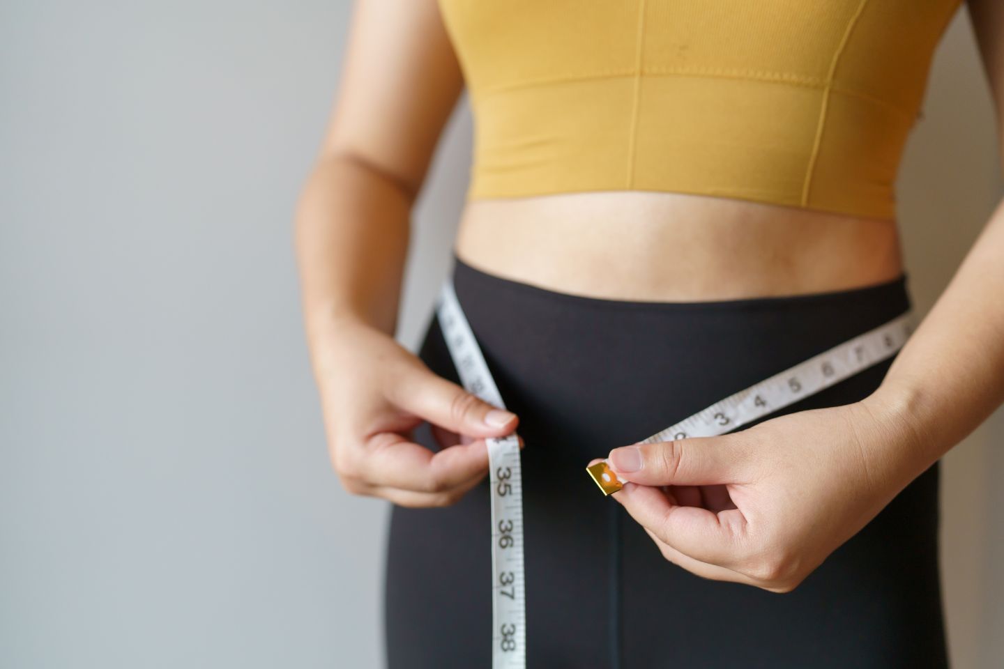 A person in a yellow top and black pants measures their waist with a tape measure, much like adjusting dynamic content for the perfect fit.